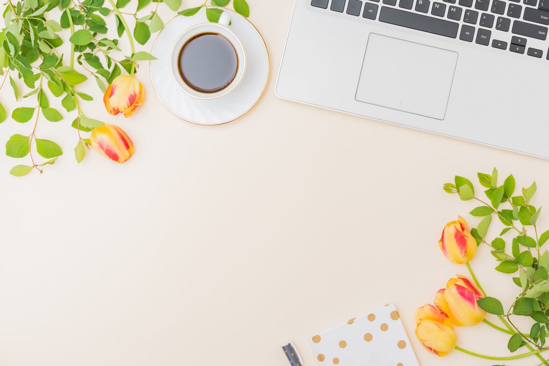 Flat lay blogger or freelancer workspace with a laptop, yellow tulips and branches with green leaves, office supplies on a color background